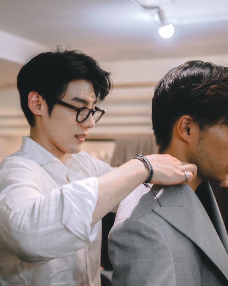 A tailor adjusting the shoulder of a jacket during a fitting